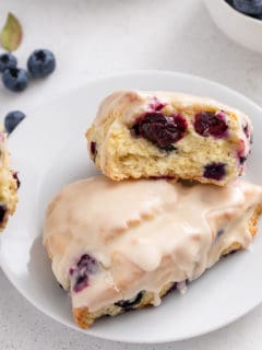 Two blueberry scones on a white plate. One of them is broken in half.
