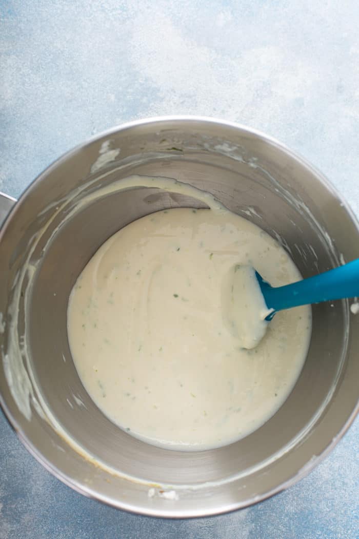 Spatula stirring together key lime cheesecake filling in a metal mixing bowl