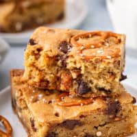 Two salted caramel blondies with pretzels stacked on a white plate