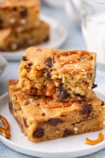 Two salted caramel blondies with pretzels stacked on a white plate