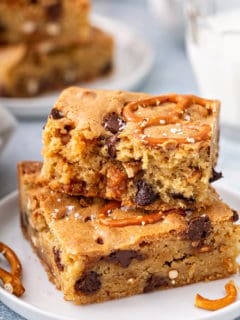 Two salted caramel blondies with pretzels stacked on a white plate