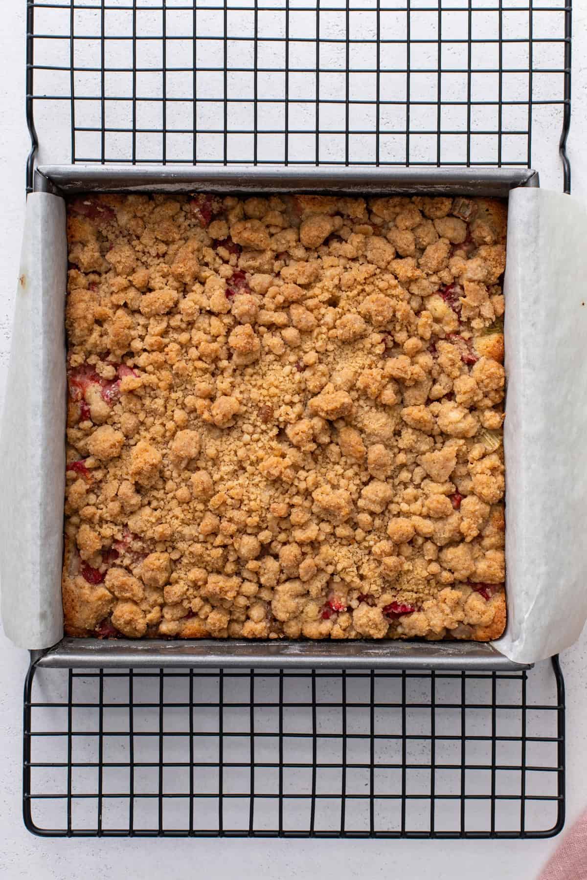 Baked strawberry rhubarb crumb cake in a square pan, cooling on a wire rack.