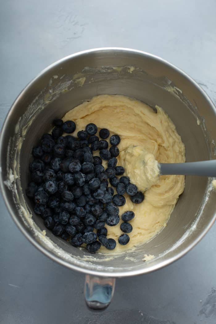 Fresh blueberries being folded into lemon bread batter in a metal mixing bowl