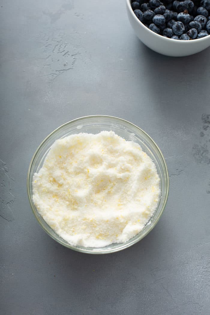 Sugar mixed with lemon zest in a small glass bowl on a gray counter