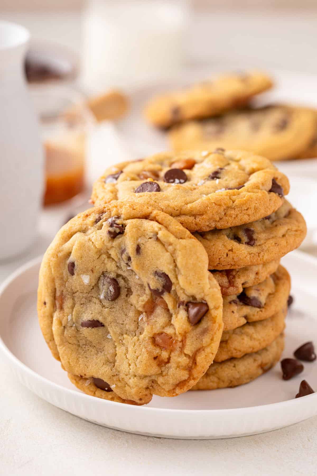 Salted caramel chocolate chip cookie leaning against a stack of the cookies on a white plate.