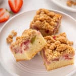 Three slices of strawberry rhubarb crumb cake on a white plate.