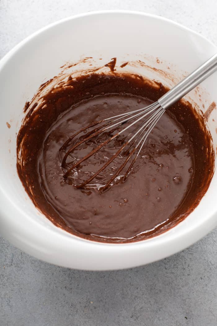 Whisk stirring batter for salted caramel brownies in a white mixing bowl