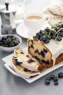 Sliced loaf of lemon blueberry bread topped with fresh blueberries on a white platter