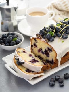 Sliced loaf of lemon blueberry bread topped with fresh blueberries on a white platter