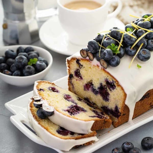 Sliced loaf of lemon blueberry bread topped with fresh blueberries on a white platter