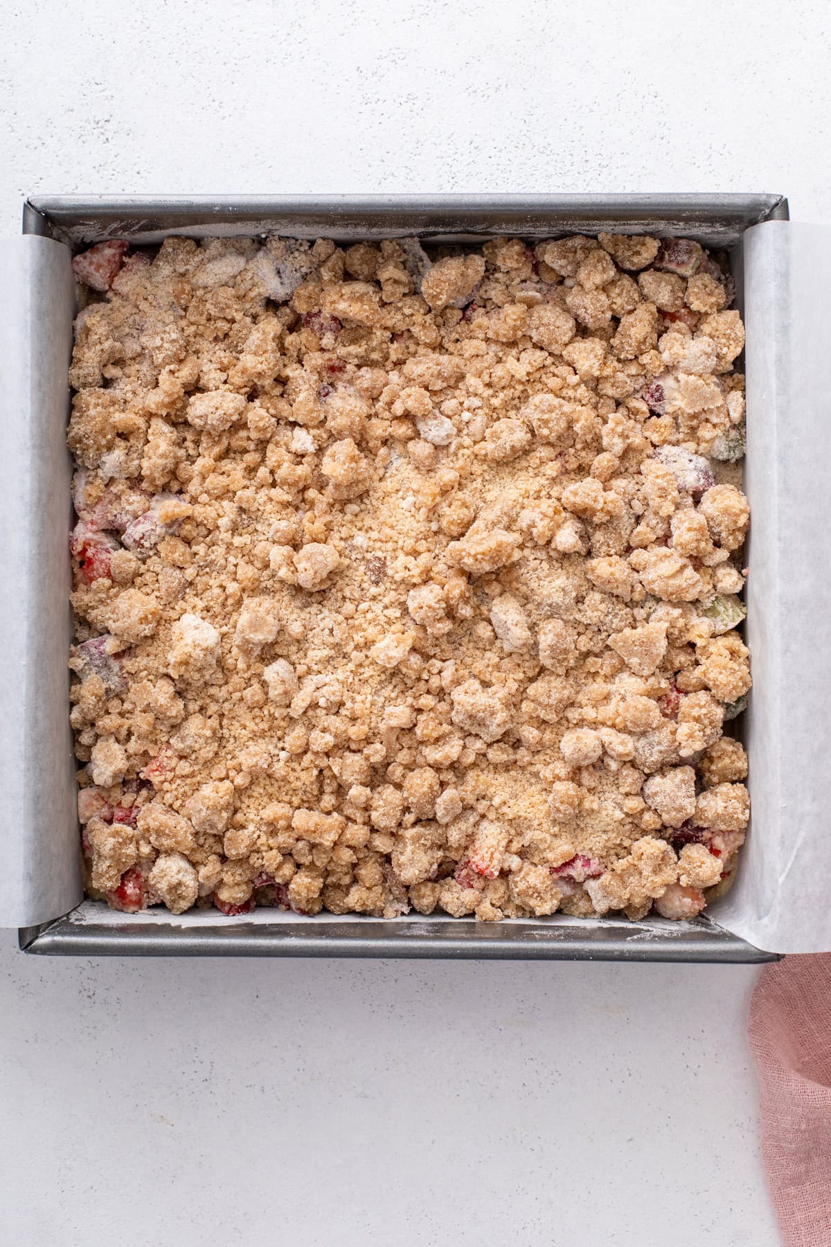 Assembled strawberry rhubarb crumb cake in a square pan, ready to go in the oven.