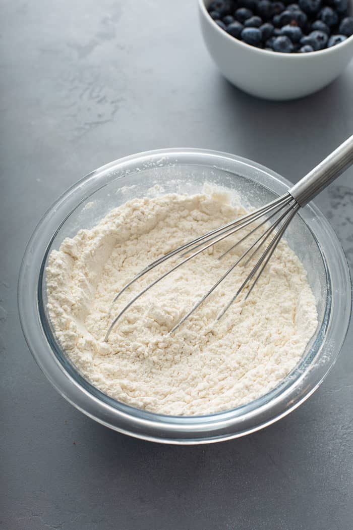 Whisk stirring together dry ingredients for lemon blueberry bread in a glass mixing bowl