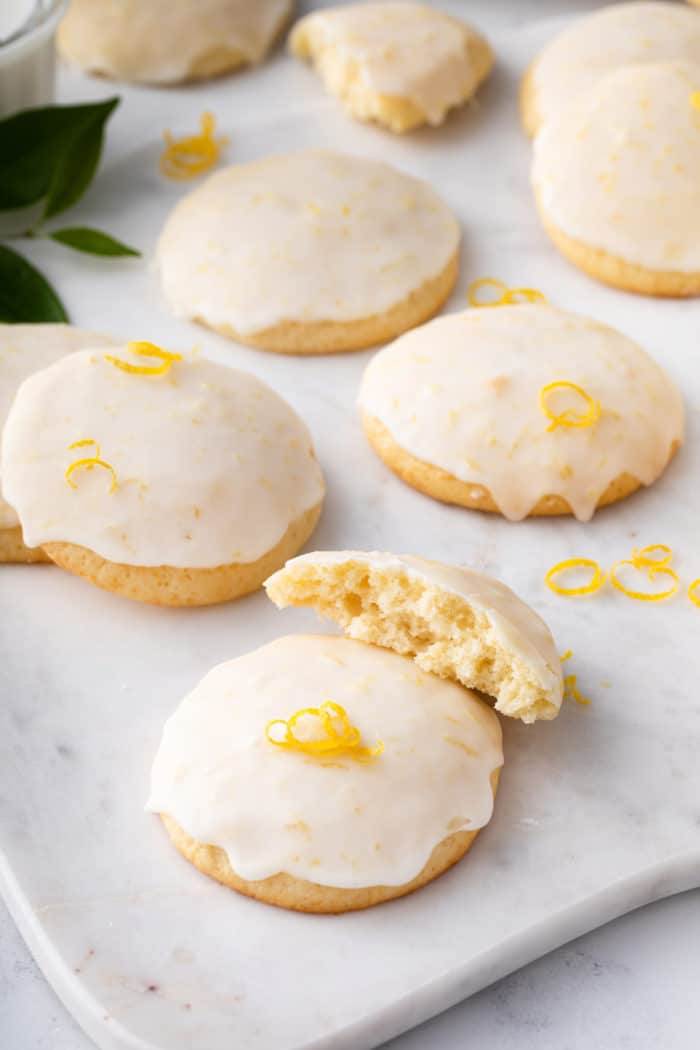 Glazed lemon ricotta cookies on a marble board. One of the cookies is broken in half.