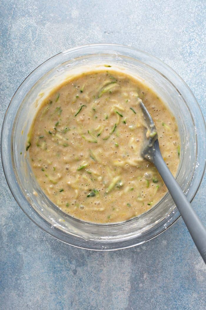 Lemon zucchini bread batter being stirred by a gray spatula in a glass mixing bowl