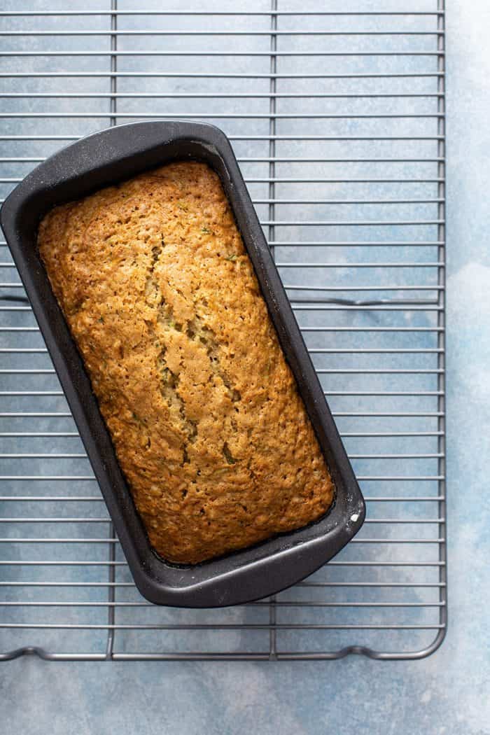 Overhead view of a freshly baked loaf of lemon zucchini bread in a loaf pan on a metal cooling rack