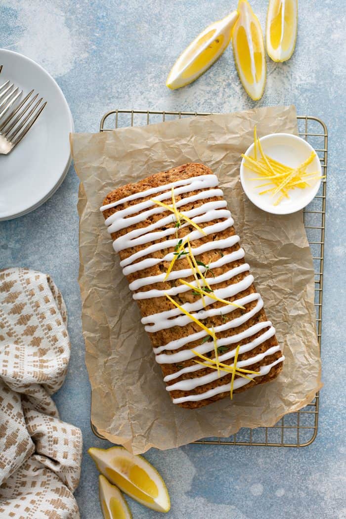 Overhead view of a glazed loaf of lemon zucchini bread on a piece of parchment paper next to a small bowl of lemon glaze