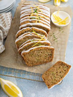 Sliced loaf of glazed lemon zucchini bread on a piece of parchment paper over a wire cooling rack