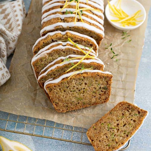 Sliced loaf of glazed lemon zucchini bread on a piece of parchment paper over a wire cooling rack