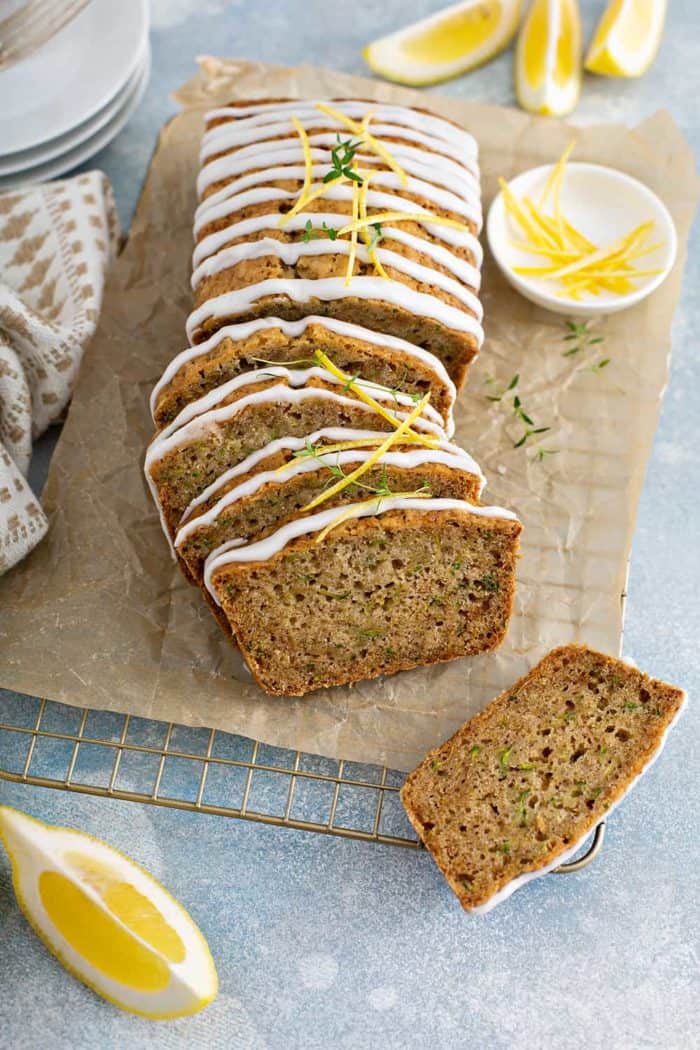 Sliced loaf of glazed lemon zucchini bread on a piece of parchment paper over a wire cooling rack