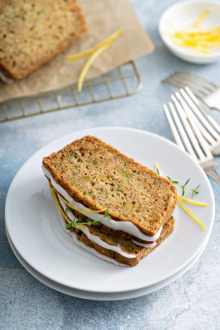 Two slices of glazed lemon zucchini bread on a white plate next to a stack of forks