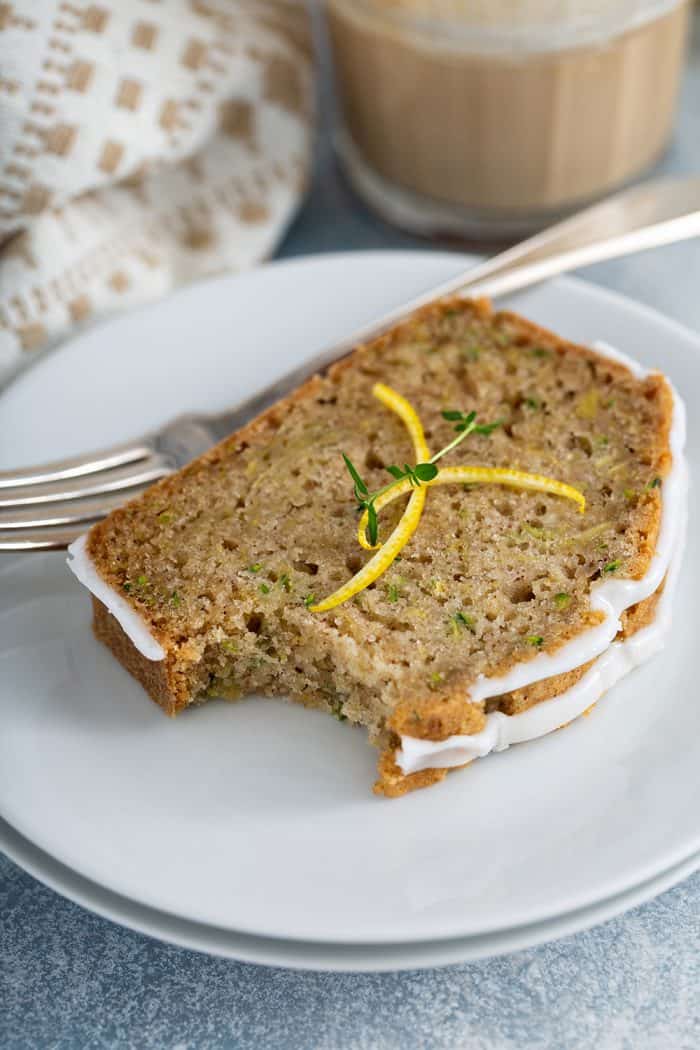 Slice of lemon zucchini bread with a bite taken out of the corner on a white plate next to a fork