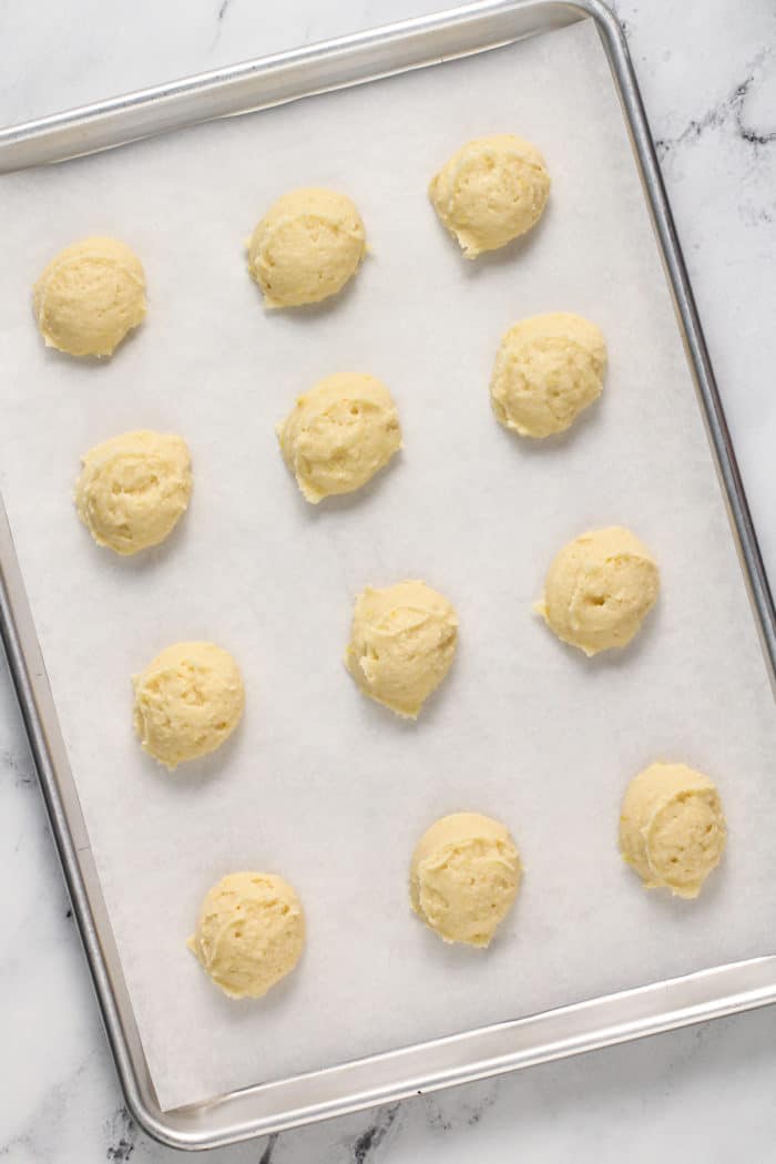 Scoops of lemon ricotta cookie dough on a parchment-lined baking sheet, ready to go in the oven.