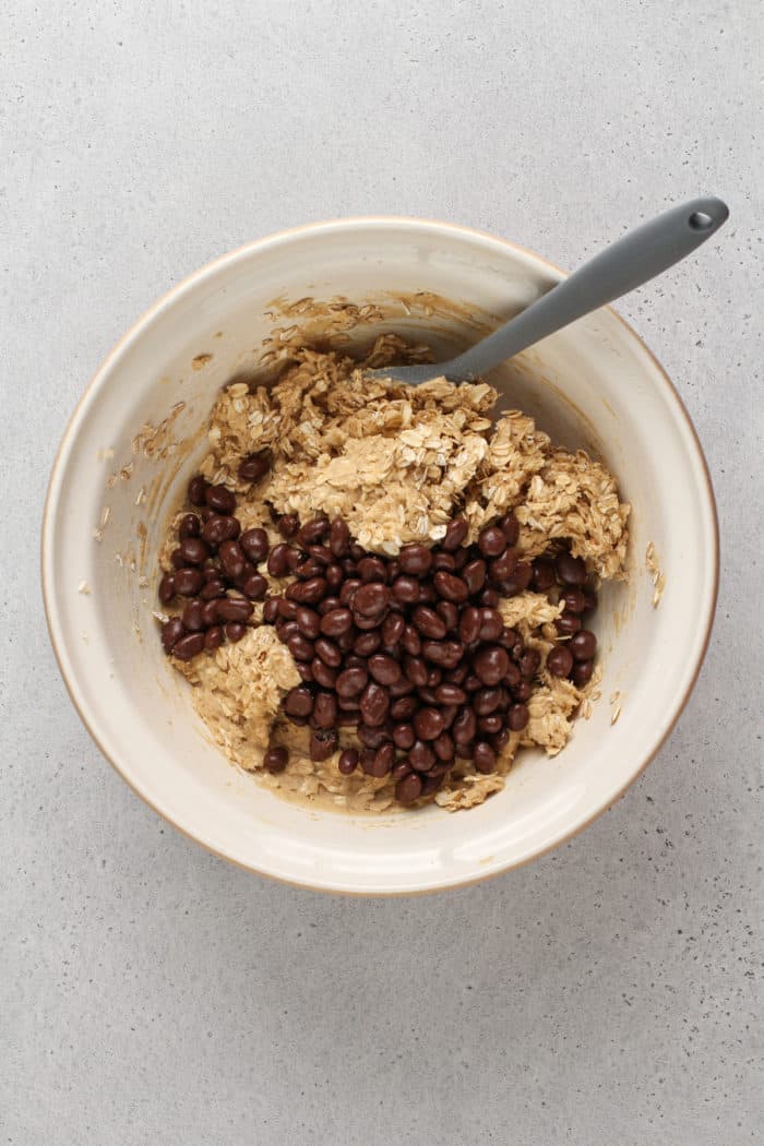 Raisinets being added to a bowl of oatmeal cookie dough.