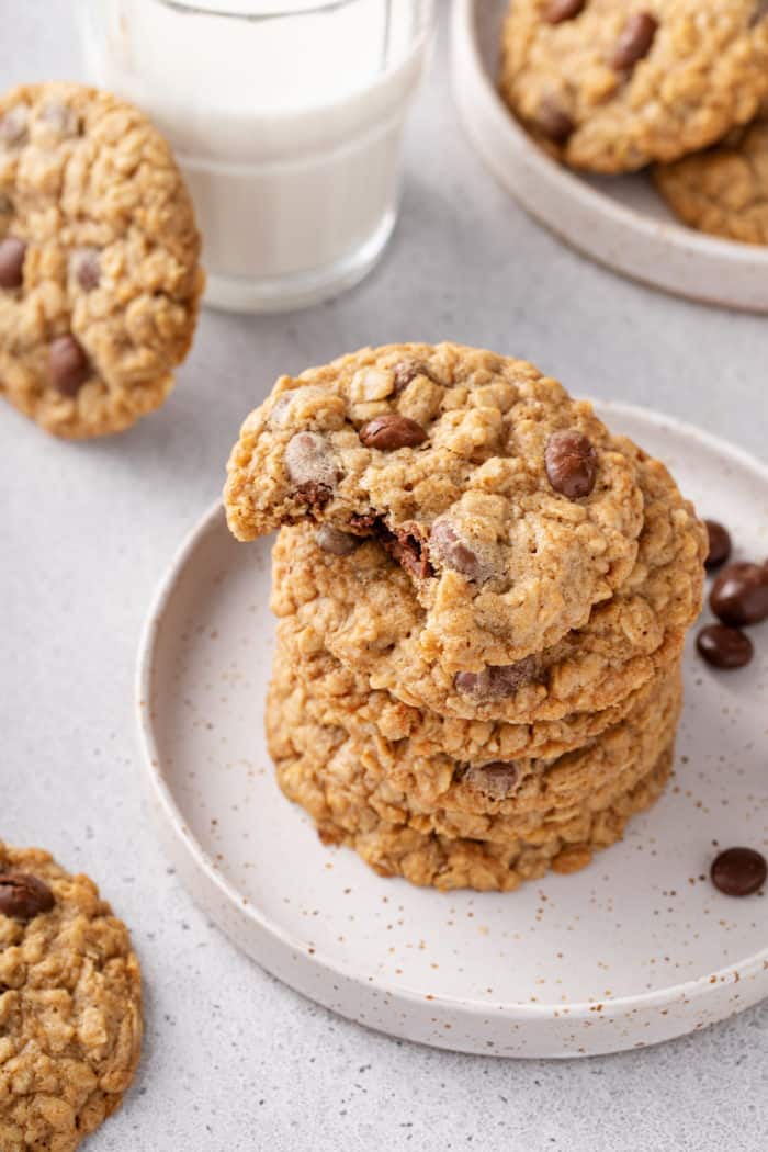 Stack of oatmeal raisin cookies on a white plate. The top cookie has a bite taken out of it.