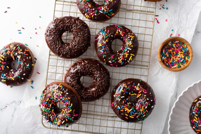 Overhead view of sprinkle-topped chocolate-glazed donuts scattered on a wire rack.