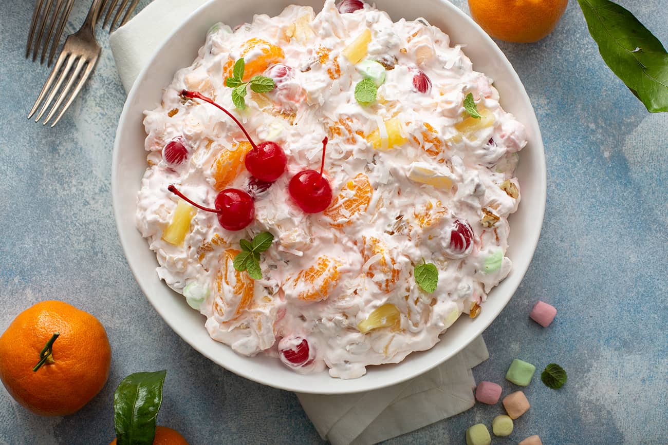 Ambrosia salad garnished with cherries in a white serving dish