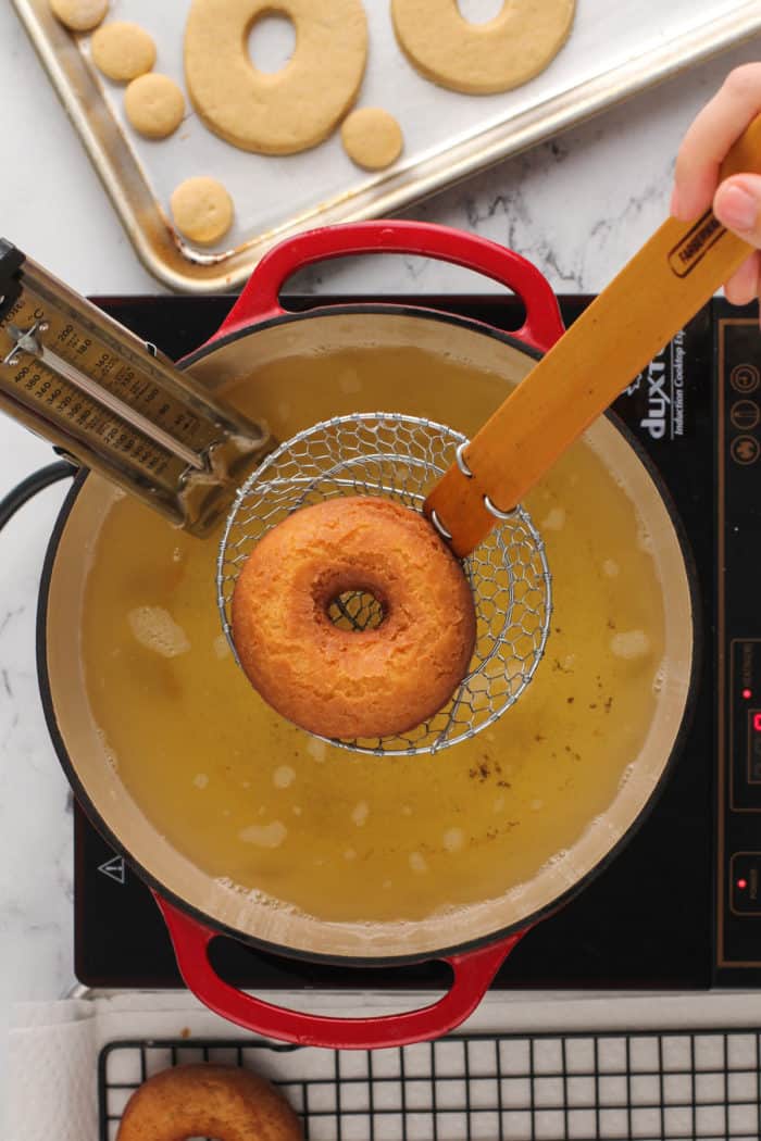 Wire spider removing a fried cake donut from a dutch oven of fry oil.