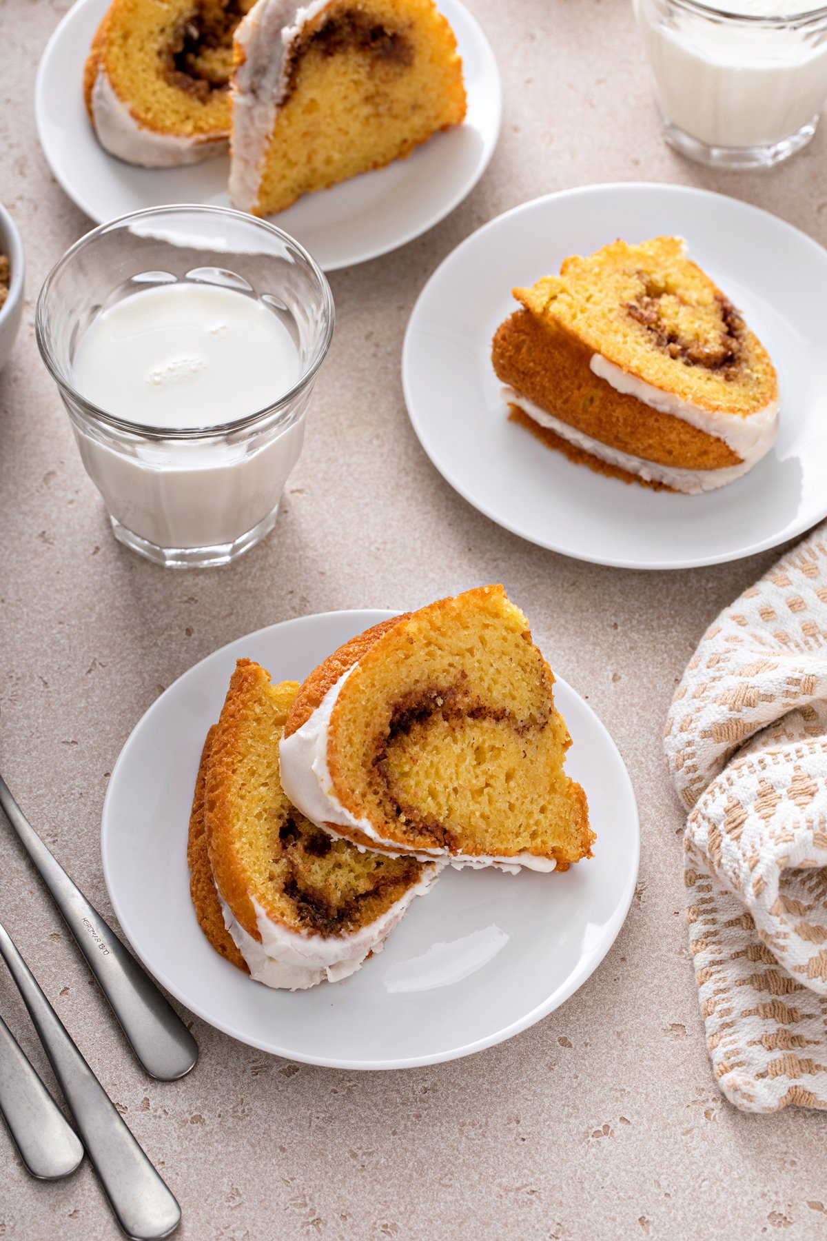 Two slices of honey bun cake on a white plate. Two more plates holding slices of cake are visible in the background.