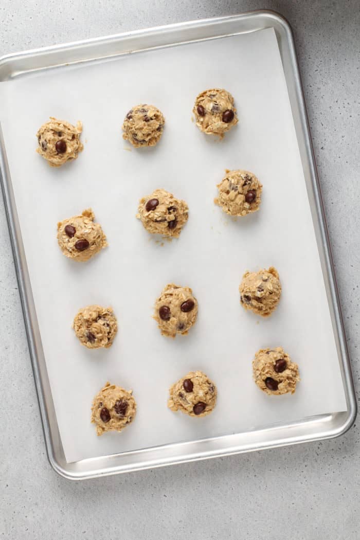 Portioned balls of oatmeal raisin cookie dough on a parchment-lined sheet tray.