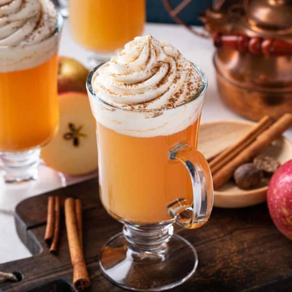 Close up of glass mug of spiced apple cider topped with whipped cream.