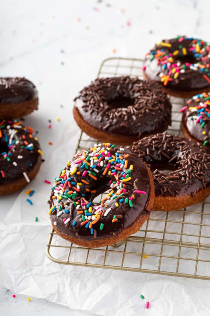 Sprinkle-topped chocolate glazed donuts scattered on a wire cooling rack.