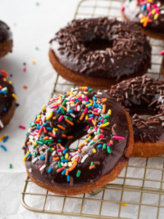 Sprinkle-topped chocolate glazed donuts on a wire rack.