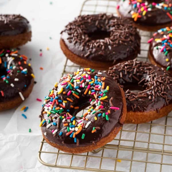 Sprinkle-topped chocolate glazed donuts on a wire rack.