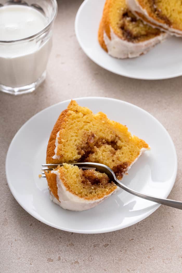 Fork cutting into a slice of honey bun cake on a white plate.