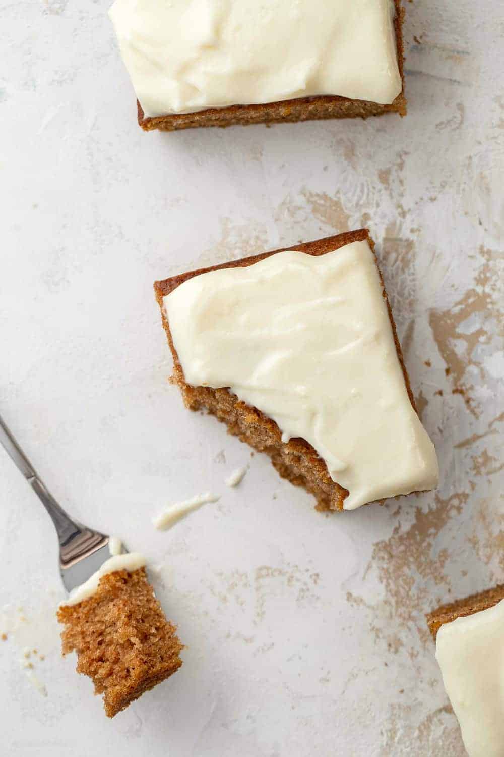 Overhead view of a fork with a bite of pumpkin bar on it, next to a sliced pumpkin bar with cream cheese frosting