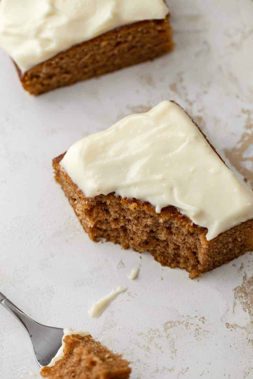 Frosted pumpkin bar with a bite taken out of it next to a fork on a white countertop