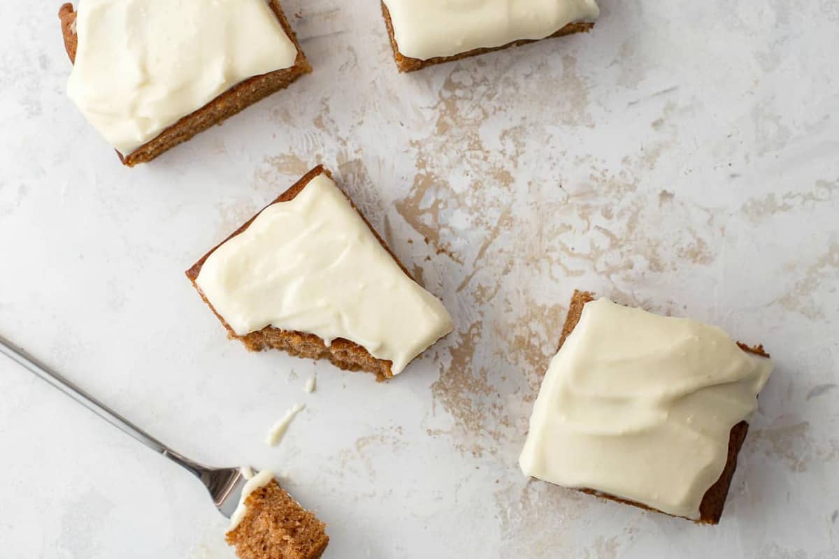 Frosted and sliced pumpkin bars scattered on a white countertop, one with a bite taken out of it