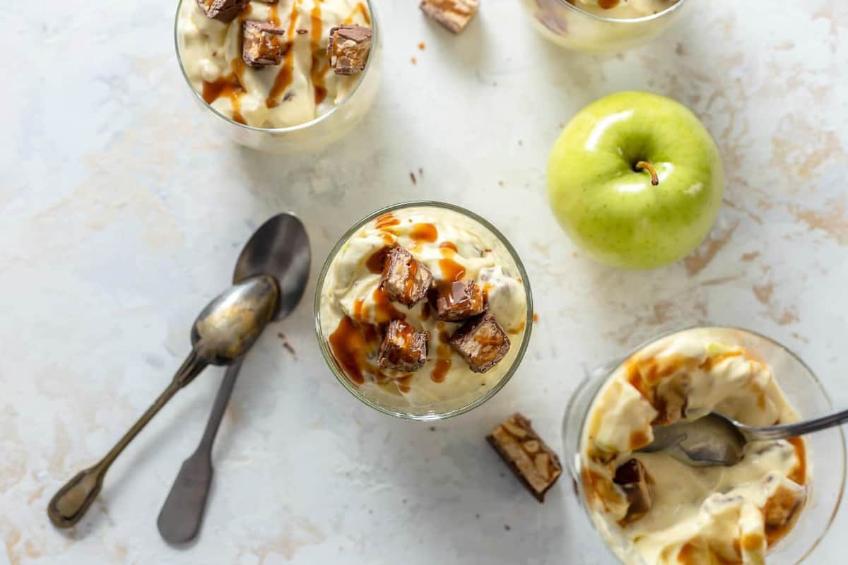 Servings of caramel apple salad in glass dishes, topped with snickers and caramel sauce