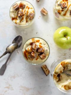 Glass dishes of Snickers Caramel Apple Salad next to candy bar pieces and granny smith apples