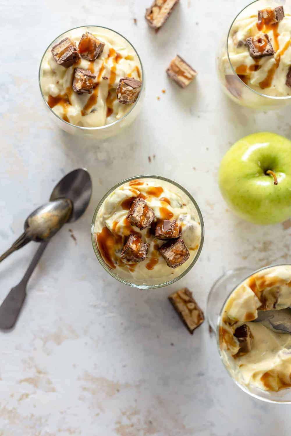 Glass dishes of Snickers Caramel Apple Salad next to candy bar pieces and granny smith apples