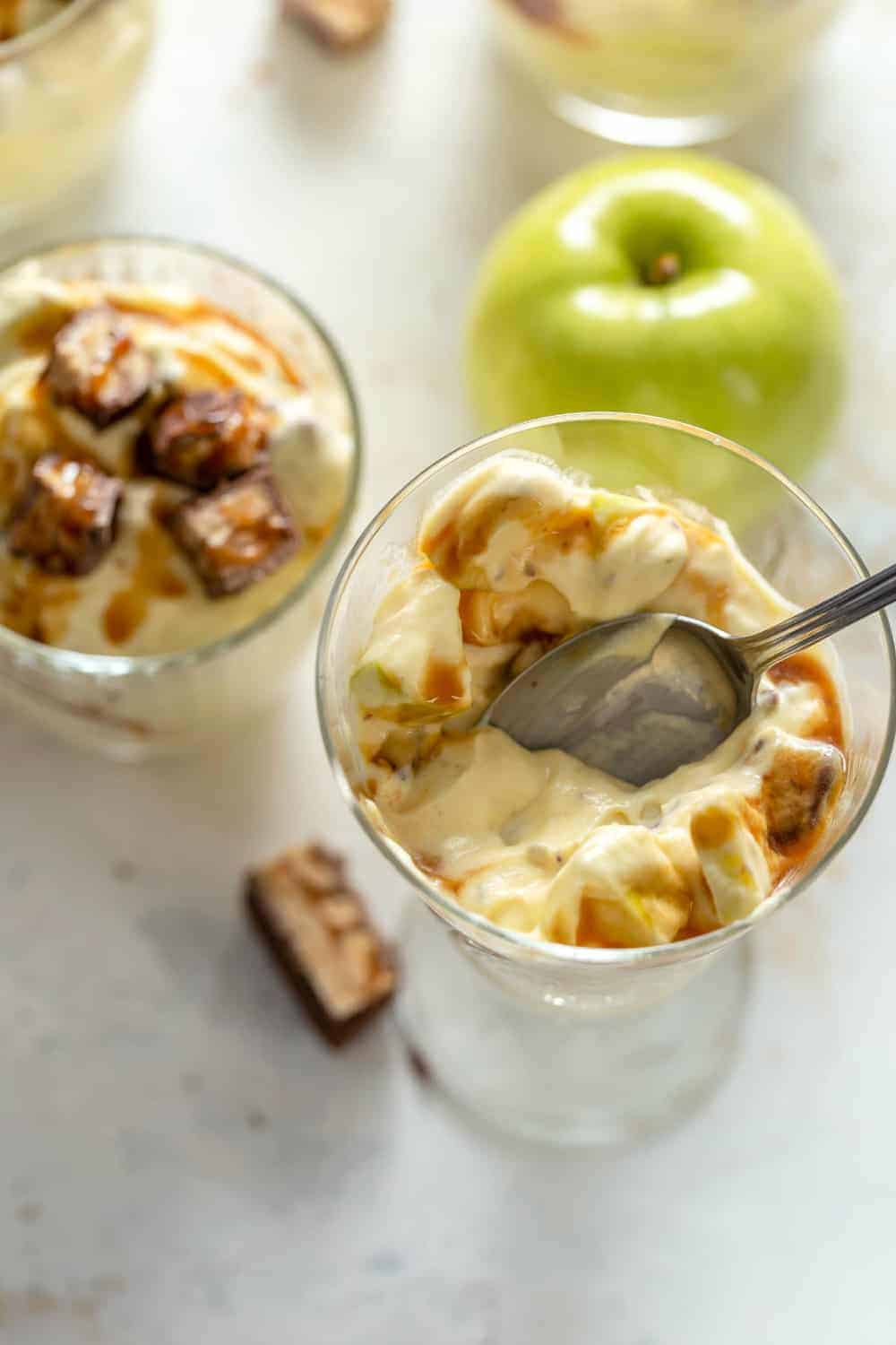 Spoon digging into a serving of Snickers Caramel Apple Salad in a glass bowl