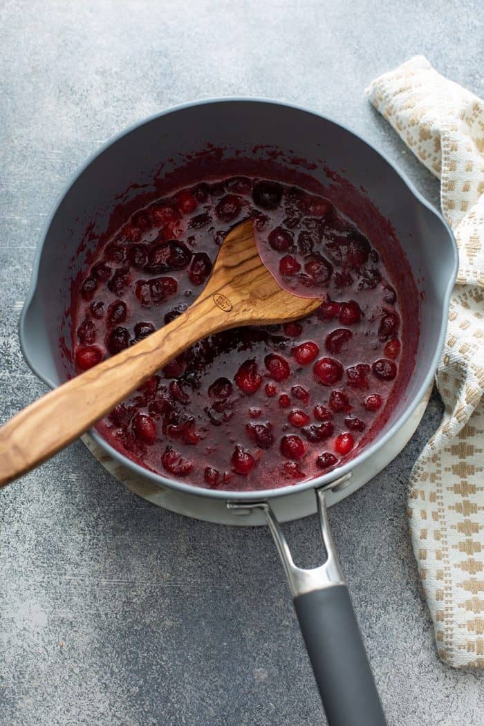 Wooden spoon stirring cooked cranberry sauce in a saucepan