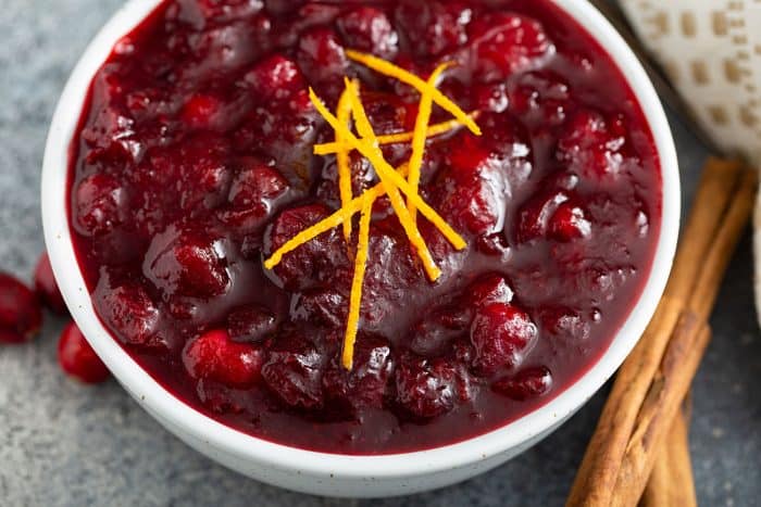 Close up of cranberry sauce in a white bowl, garnished with orange zest