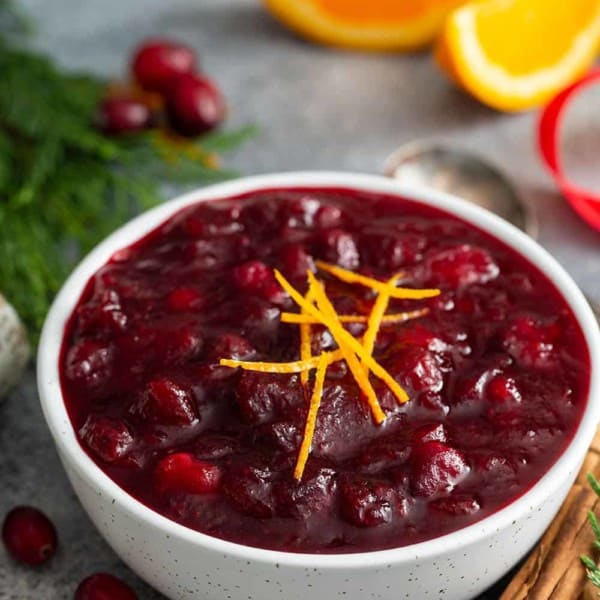 Cranberry sauce in a white bowl, surrounded by greenery and cinnamon sticks
