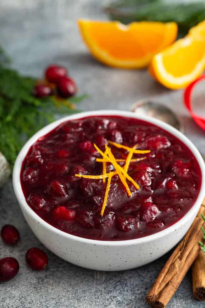 Cranberry sauce in a white bowl, surrounded by greenery and cinnamon sticks