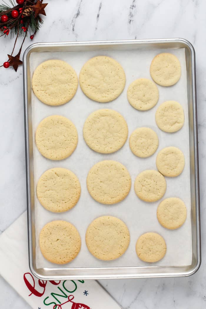 Baked sugar cookies on a lined baking sheet for melted snowman cookies.